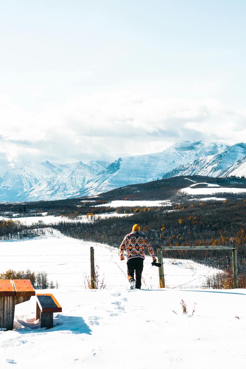 Person walking through fresh snow toward the Rocky Mountains near Waterton Lakes, Alberta, wearing a patterned winter sweater and yellow toque. captured by photographer Ali Kazal
